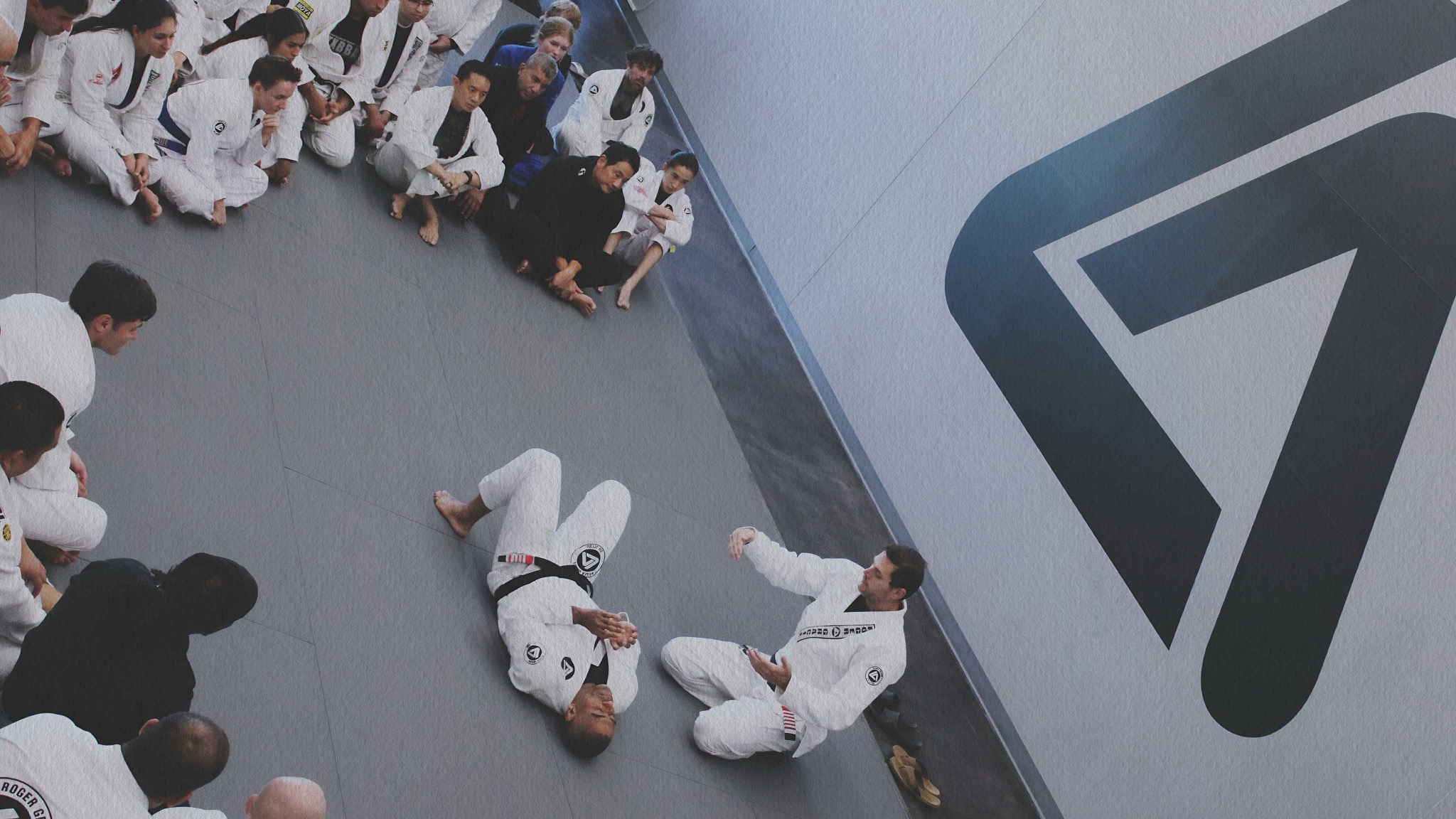 Adults of a range of ages seated around the mat during instruction at Roger Gracie Academy Frisco